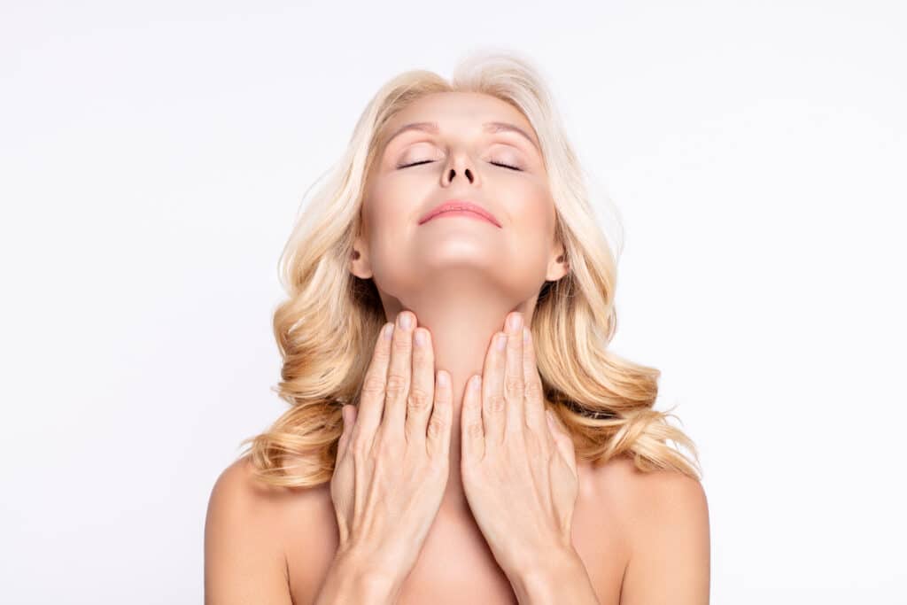 Beautiful older woman touching her neck and smiling after getting a neck lift to reduce sagging, loose skin.